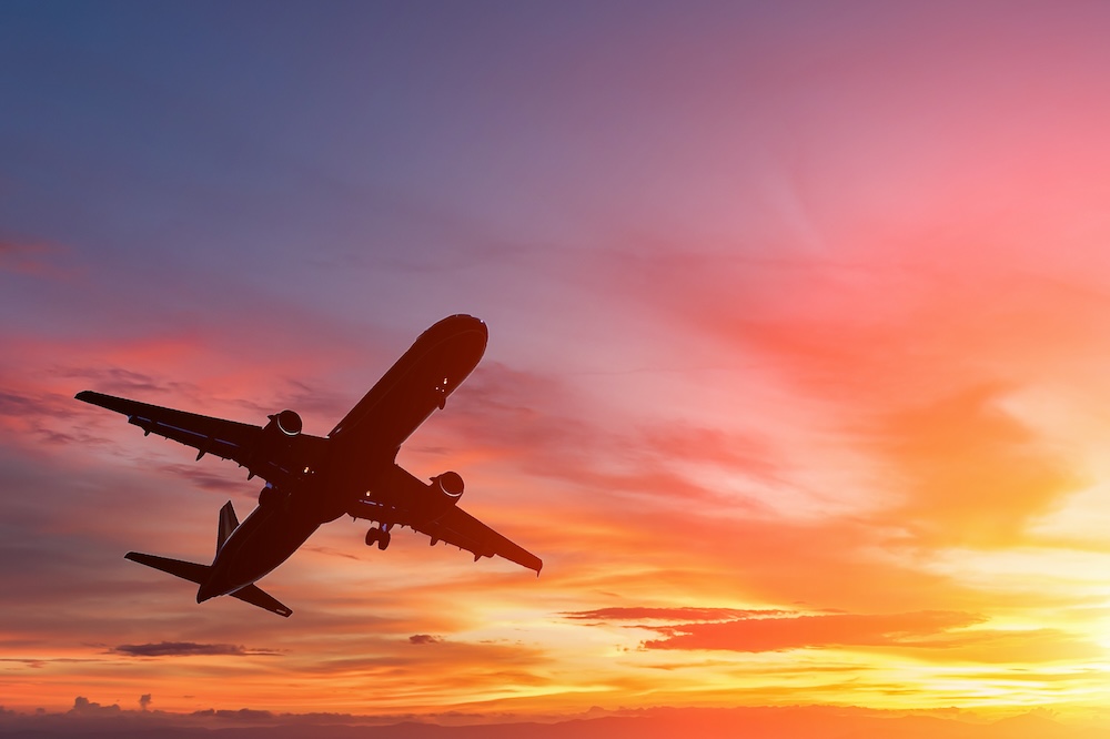 The silhouette of a passenger plane flying in sunset.
